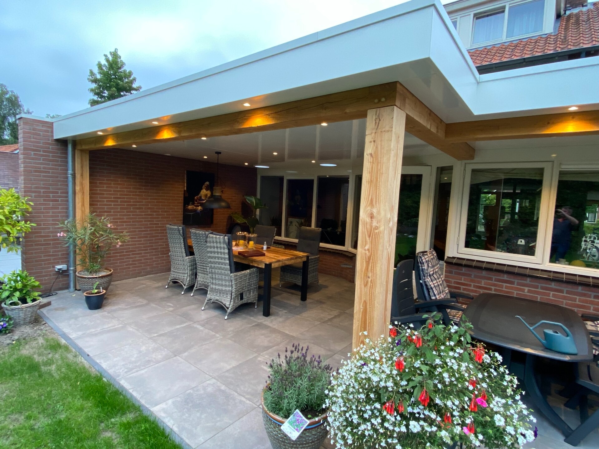 Overdekt terras van woning in Delden met eiken overkapping, verlichting en bloemen
