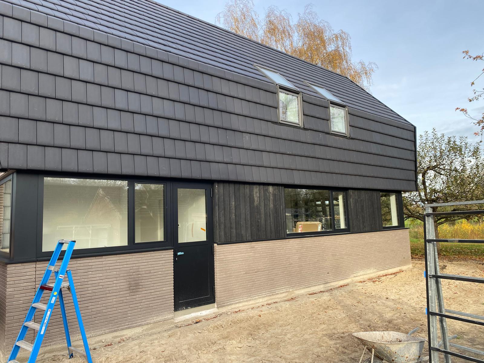 Zijaanzicht van de vrijstaande nieuwbouw woning aan de Goorsestraat in Hengevelde met donkere dakbekleding, houten gevelbekleding en licht metselwerk.