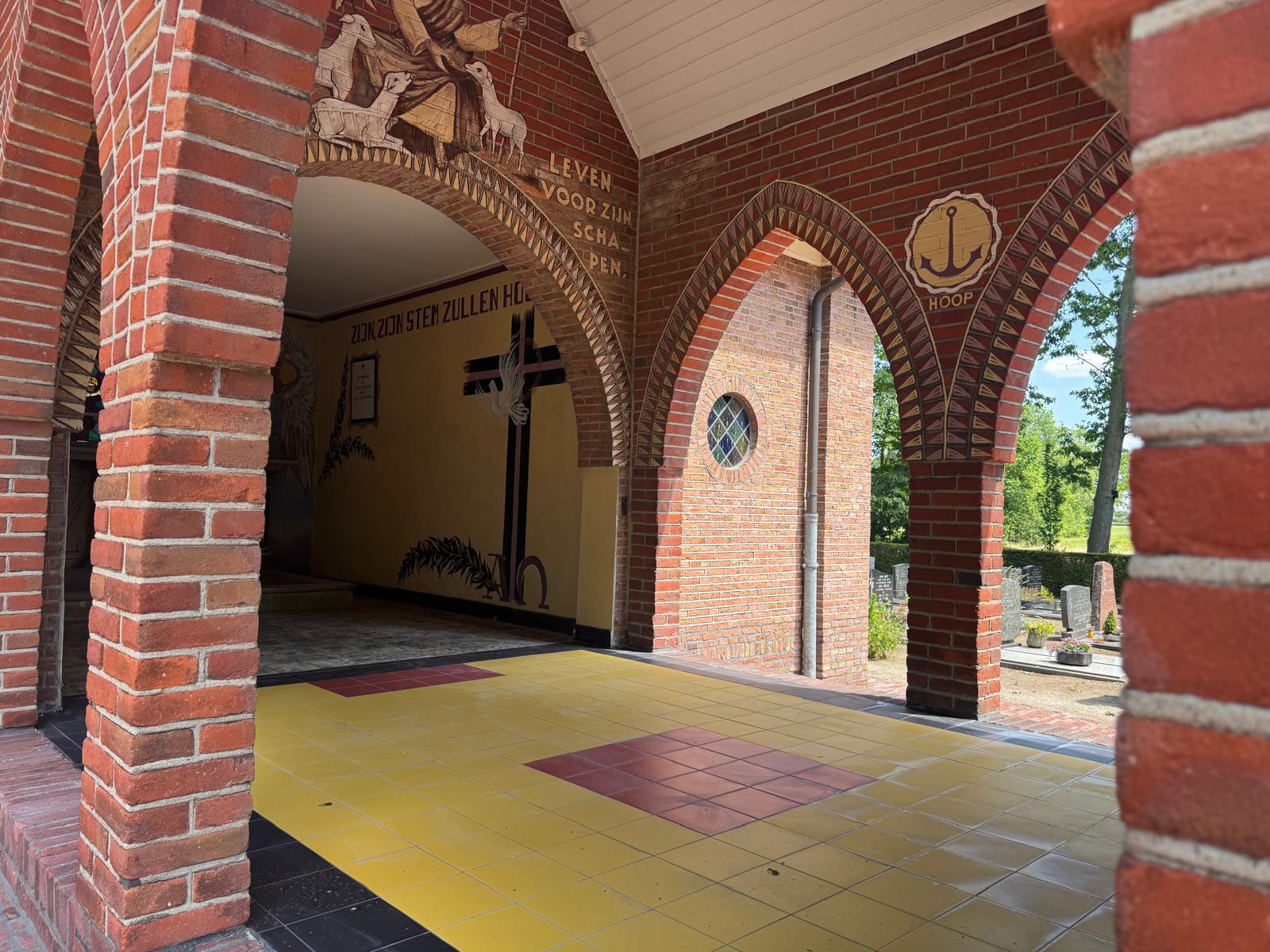 Overdekte entree van de historische kapel met gerestaureerd metselwerk, tegelvloer en schilderwerk.