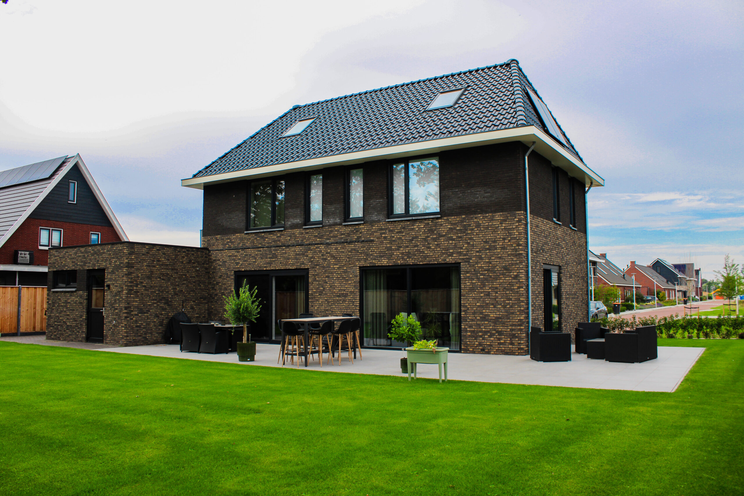 Achterzijde van de nieuwbouwwoning met ruime tuin, terras en donkere bakstenen gevel