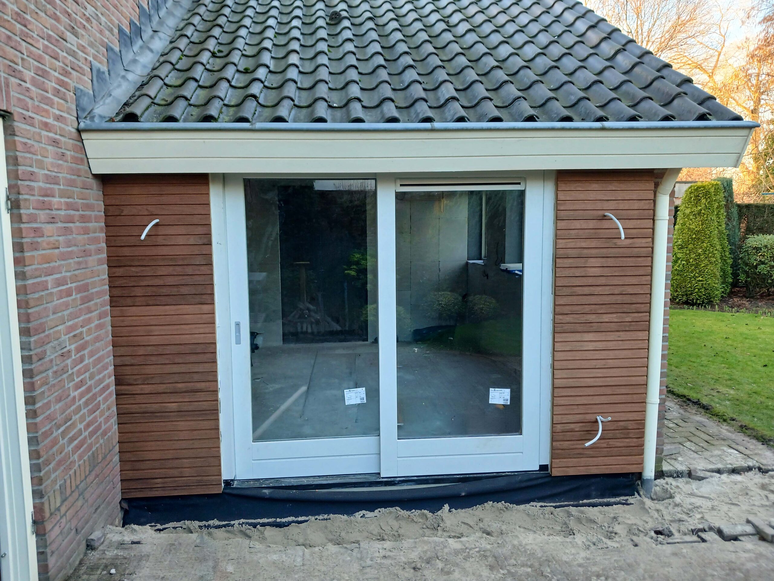 Aanbouw met houten gevelbekleding, witte schuifpui en pannendak bij een woning in Eibergen