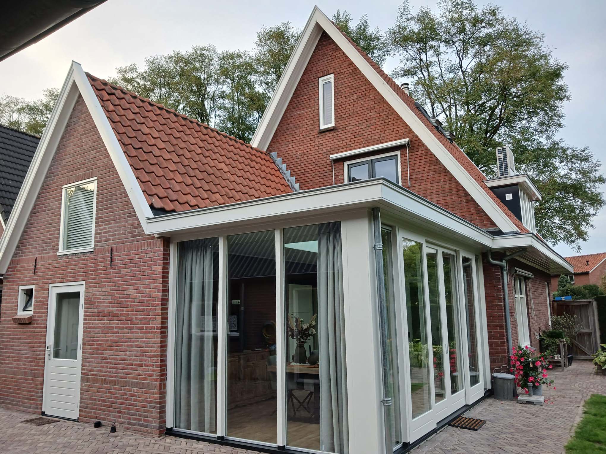 Aanbouw met grote raampartijen en witte kozijnen aan een bestaande woning