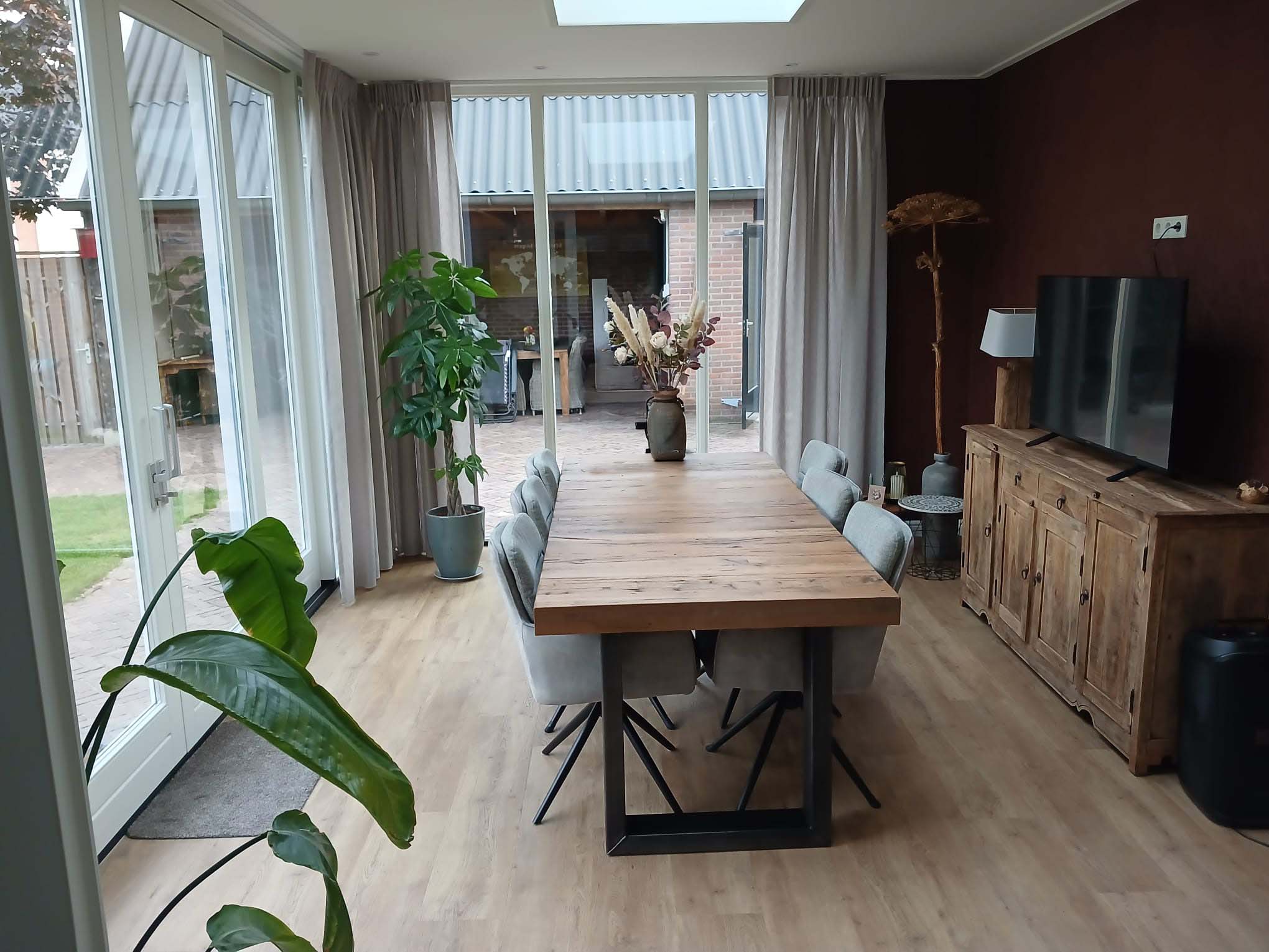 Eetkamer met houten eettafel en grote glazen schuifpui in Neede