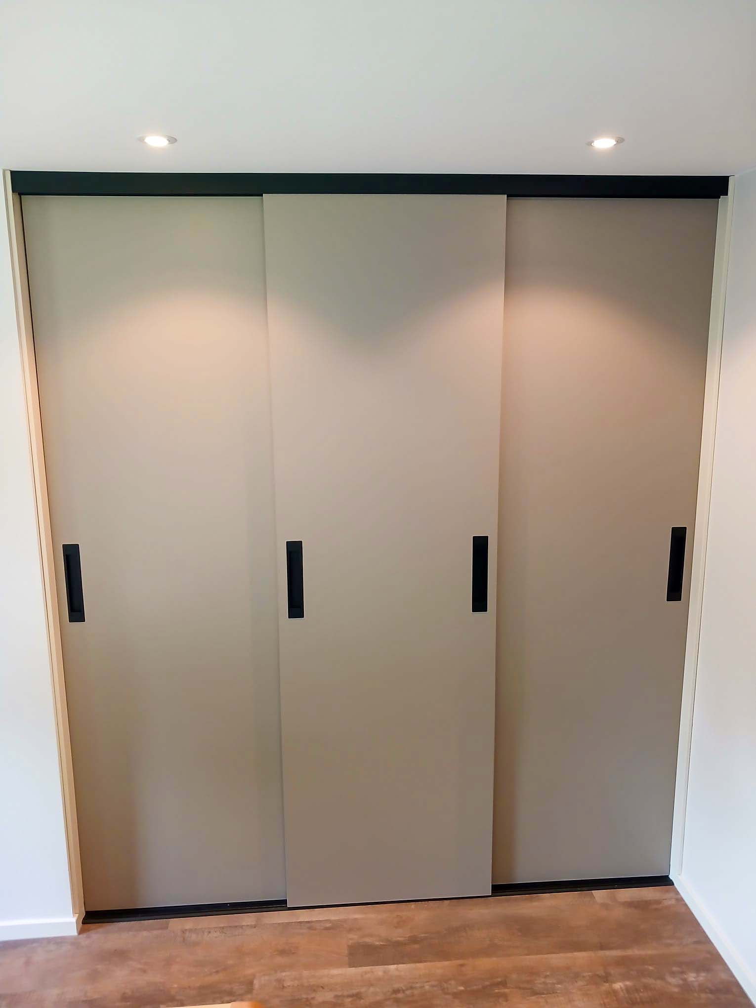 Ingebouwde schuifdeurkasten met beige deuren en zwarte handgrepen in een slaapkamer