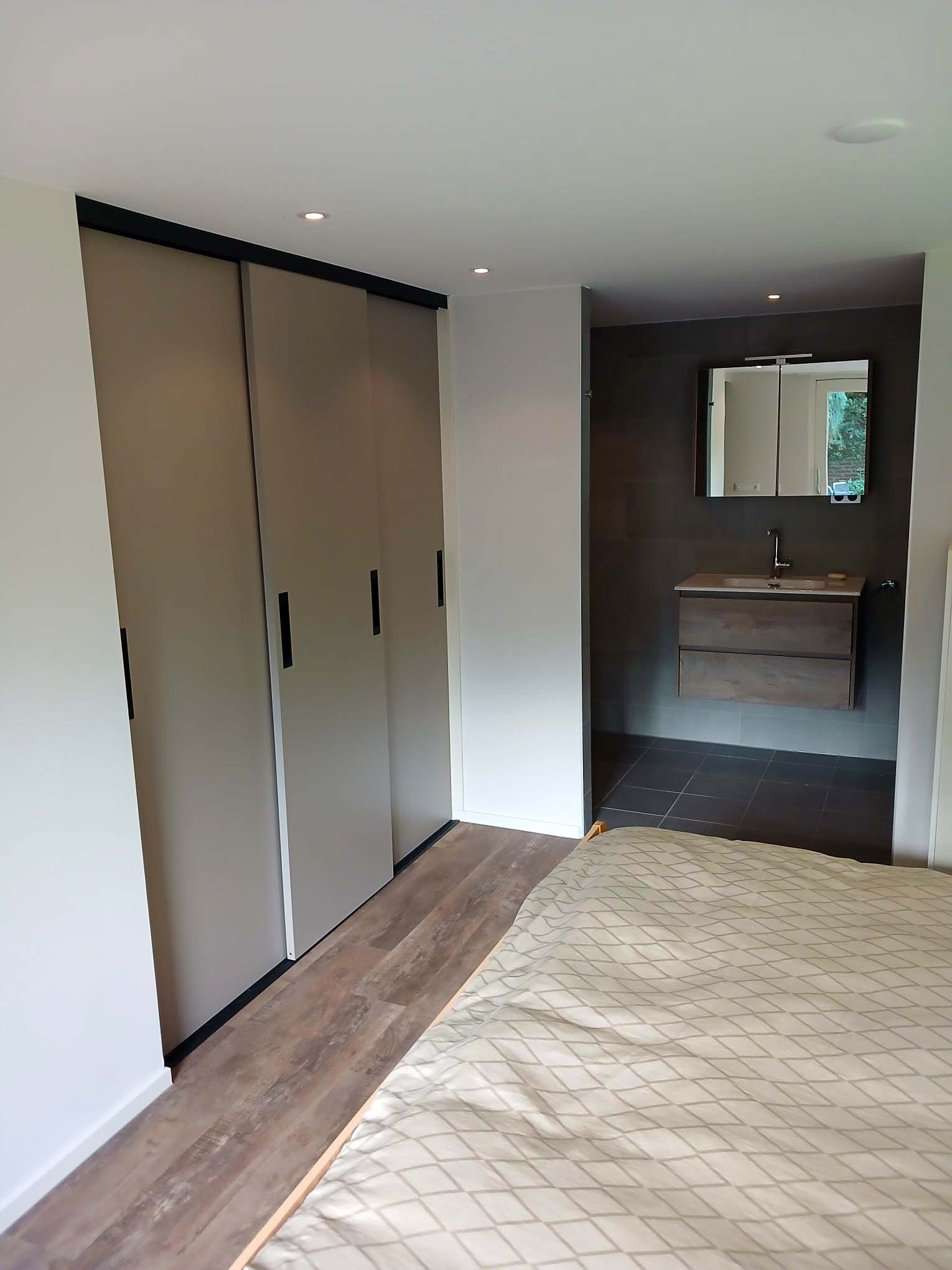 Slaapkamer met ingebouwde maatwerkkasten, houten vloer en aangrenzende badkamer