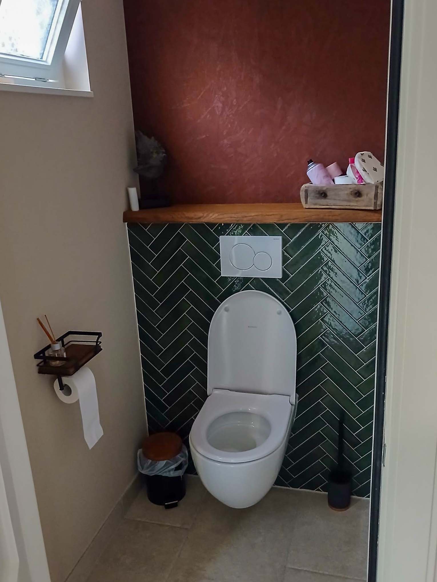 Toilet met groene visgraattegels, houten plank en hangend toilet
