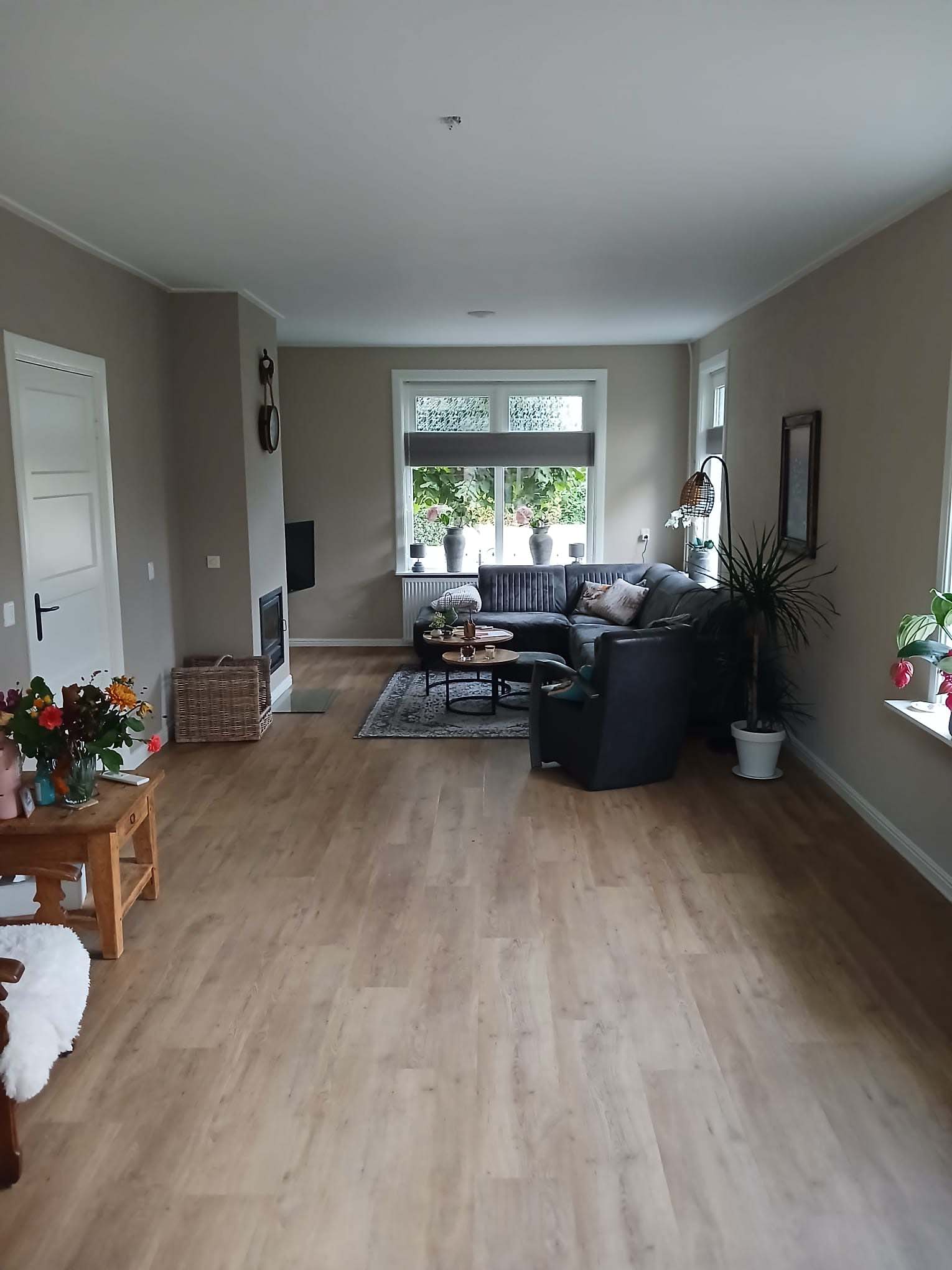 Woonkamer na verbouwing met nieuwe vloer, zithoek en moderne afwerking